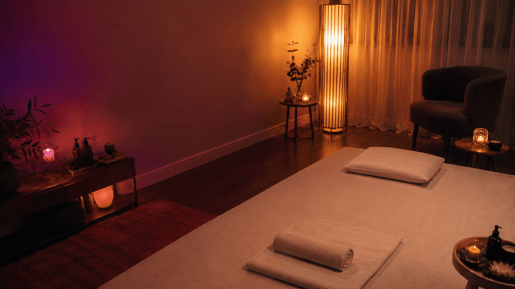 Sala sensorial de massagem com colchonete no chão, luminária, velas e luzes coloridas